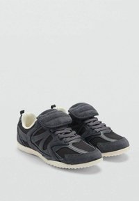 Sive atletske cipele s mrežastim i antilop panelima, s čičak trakama i teksturiranom gumenom potplatom. Dizajnirane za udobnost i podršku.