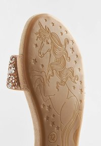 Suola di sandalo con un unicorno in rilievo circondato da stelle e una tracolla scintillante decorata con strass su uno sfondo beige.