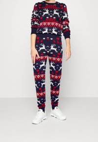 Mörkblå jultröja och matchande byxor. Har röda hjärtan, renar och snöflingor i ett stickat mönster. Kombineras med vita sneakers.