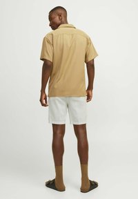 Chemise en polyester beige à manches courtes, avec une coupe décontractée, associée à un short en lin blanc. Dispose d'un col pointu et de détails de couture au dos.