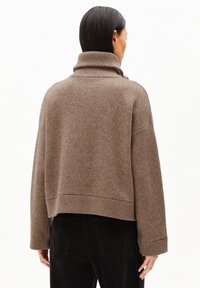Brun, stickad tröja med hög krage, sänkta axlar och ribbade ärmslut. Har en avslappnad passform och mjuk textur.