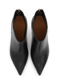 Botas de cuero negras hasta el tobillo con punta afilada, textura suave y cremalleras laterales. El interior cuenta con una plantilla marrón. Diseño minimalista.
