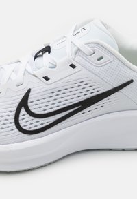 Bijela atletska cipela s prozračne mrežaste gornje strane, crni Swoosh akcent, ravne vezice i udoban jastučićat potplat.