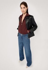 Svart läderjacka över en vinröd zip-up hoodie, kombinerad med ljusblå vida jeans och spetsiga beige skor. Slät textur och modern design.