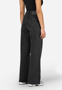 Crne široke traperice s visokim strukom, s stražnjim zasebnim džepom i kontrastnim šavovima. Nosite ih s uskim crnim topom i tenisicama.