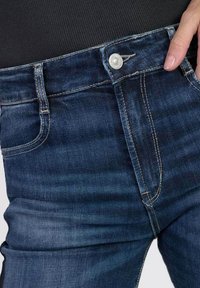 Donkerblauwe denim jeans met een getailleerd ontwerp. Voorzien van een knoopsluiting, voorzakken en contrasterende stiksels. Soepele textuur.