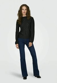 Top nero a maniche lunghe con design testurizzato e maniche a sbuffo, abbinato a jeans svasati blu scuro e scarpe nere.