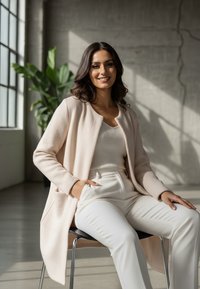 Jasnoróżowy, fakturowany kardigan z zaokrąglonym dekoltem, nałożony na biały prążkowany top i kremowe spodnie, osoba siedzi na krześle w jasnym pokoju.