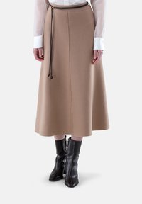 Beige Midi-Rock aus weichem Stoff, mit geradem Schnitt, Gummizug in der Taille und kombiniert mit schwarzen Ankle Boots.