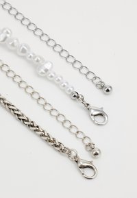 Four chains: silver metal links, one with glossy white pearls, a braided design, and differing clasp styles. Smooth and shiny textures.