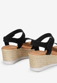 Sandalias de cuña de ante negro con suela envuelta en yute y una suela de goma blanca texturizada. El diseño de las correas proporciona un ajuste seguro.