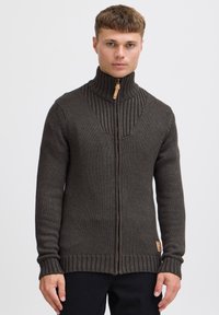 Maglione zip-up marrone scuro con colletto alto, design a coste sulle spalle e lavorazione a maglia testurizzata. Presenta un'etichetta in pelle sul lato inferiore.
