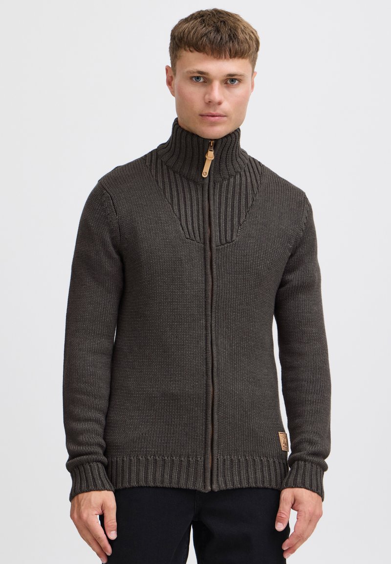 Maglione zip-up marrone scuro con colletto alto, design a coste sulle spalle e lavorazione a maglia testurizzata. Presenta un'etichetta in pelle sul lato inferiore.