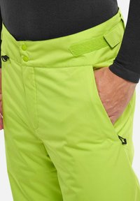Helle grüne Skihose mit glatter Textur, zwei Knopfverschluss und Klettverschlussanpassung am Bund. Seitliche Taschenoptik sichtbar.
