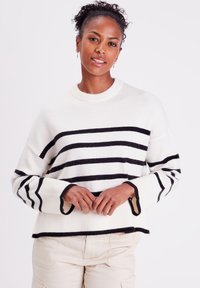 Pull rayé blanc avec des lignes navy, doté d'un col rond et de poignets côtelés avec des finitions contrastées. Texture en maille douce.