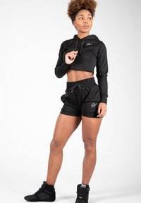 Zwarte cropped hoodie met logo, bijpassende zwarte shorts met elastische tailleband en zwarte hoge sneakers. Gladde textuur, casual sportieve design.