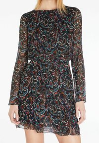 Langärmeliges, schwarzes Kleid mit einem bunten Paisley-Muster. Der Stoff ist transparent mit einer fließenden Silhouette und einer gerafften Taillendetail.