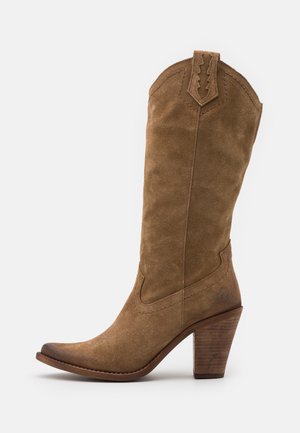 Bota vaquera de ante marrón con punta afilada, detalles cosidos y tacón alto de madera. Presenta un diseño decorativo en la parte superior y textura suave.