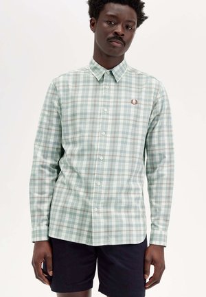 Hellgrünes kariertes Longsleeve-Shirt mit weißen und braunen Akzenten, ausgestattet mit einem Button-Down-Kragen und einem bestickten Logo auf der Brust.