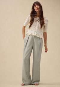 Lace white blouse with short sleeves and button closure, paired with high-waisted, light gray, wide-leg trousers featuring pleats.