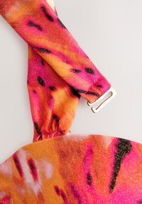 Sangle en tissu rose vif et orange avec des taches noires et une boucle en plastique blanc, partie d'un vêtement ou accessoire à motifs.