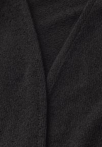 Svart stickad tyg med en mjuk textur, med en V-formad krage och varierande mönster av stickade sömmar. Nära vy.