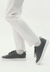 Grå sneakers med vita sulor, rund tå och platta snören. Har en hälpulltab. Matchas med vita byxor och ljusa strumpor.