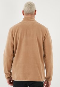 Giacca in pile color panna con colletto alto, maniche lunghe e una texture morbida. Presenta un orlo dritto e nessun hardware visibile.
