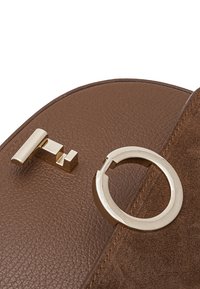 Braune Lederhandtasche mit glatter Textur, runder goldener Hardware und einem geometrischen Verschlussdetail.