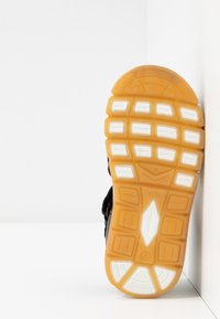 Černá sportovní podešev s žlutou gumou a bílými texturovanými akcenty; obsahuje segmentovaný design a výrazný vzor záběru.