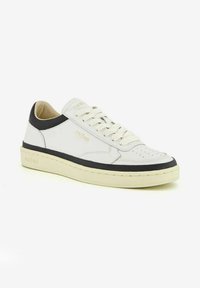 Sneaker in pelle bianca con dettagli neri, punta rotonda e decorazioni perforate. Presenta una suola beige chiaro e un'inconfondibile marca "Ghoud".