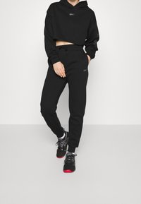 Svart kort hoodie med långa ärmar och logotyp, kombinerad med matchande svarta joggers med elastisk midja och sidfickor.