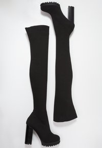 Medias negras por encima de la rodilla con un tejido de punto texturizado, un tacón alto y una suela de plataforma, diseñadas para un ajuste ceñido.