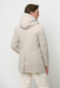 Ljusbeige vattentät jacka med huva, som har en ryggventil, en stilren design och en mjuk textur. Idealisk för avslappnad användning i milt väder.