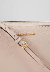 Ljusrosa läderhandväska med texturerad yta, guldhardware och avtagbar rem. Har den präglade logotypen "MICHAEL KORS."