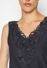 Top sem mangas preto com intrincados bordados florais na gola em V, com uma textura suave e macia e detalhes sutis de renda.