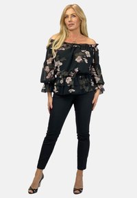 Czarna blouse z kwiatowym wzorem, z dekoltem off-the-shoulder, falbankowymi rękawami i elastycznym paskiem. Połączona z dopasowanymi czarnymi spodniami i czarnymi szpilkami.
