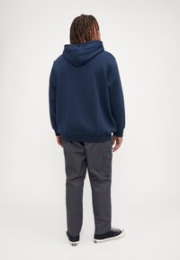 Mørkeblå hettegenser med snøring, kombinert med grå cargo-bukser med sidelommer og svarte joggesko med hvite såler.
