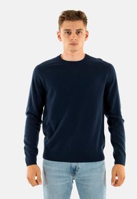 Maglione girocollo blu navy realizzato in tessuto morbido, con maniche lunghe e polsini a coste, abbinato a jeans azzurri.