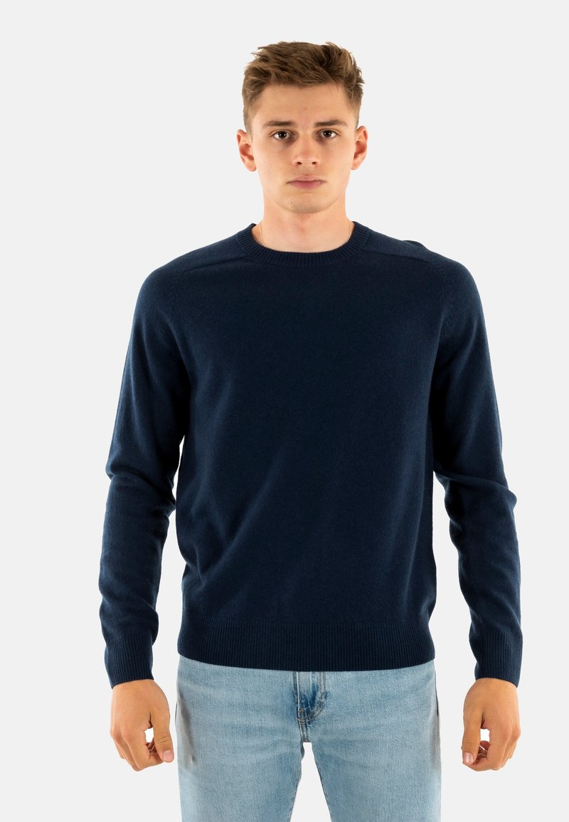 Maglione girocollo blu navy realizzato in tessuto morbido, con maniche lunghe e polsini a coste, abbinato a jeans azzurri.