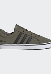 Zapatilla baja verde oliva con rayas negras, cierre de cordones, lengüeta acolchada y suela de goma blanca con franja negra de acento.