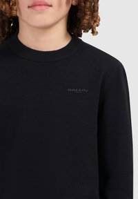 Zwarte gebreide trui met een geribde hals en subtiele "BALLIN" logo in bijpassend zwart, aansluitend ontwerp, gladde textuur.