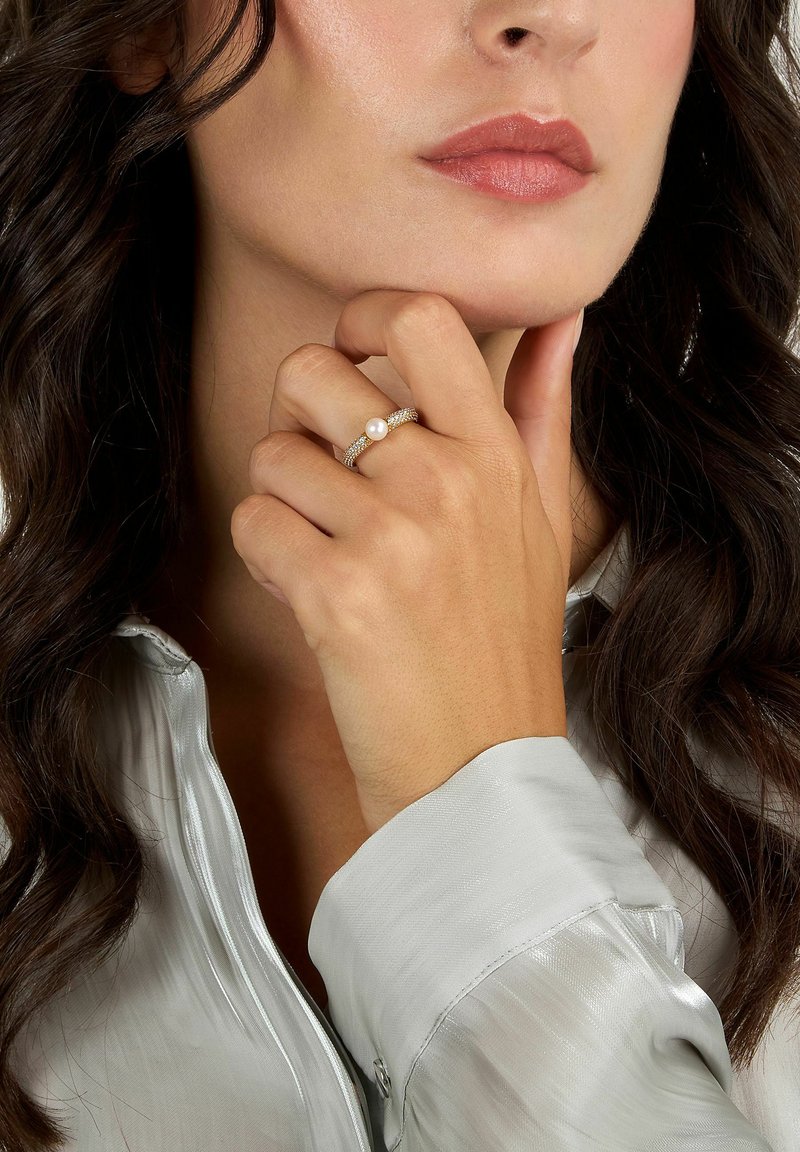 Anello d'argento con una perla, caratterizzato da una fascia texturizzata. Indossato su una mano con manicure neutra, su una leggera blusa di seta.