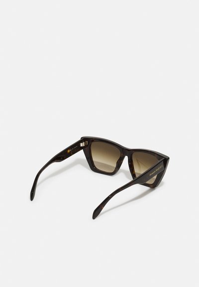 Tortoiseshell sunglasses with a angular cat-eye design and gradient brown lenses. Gold branding on the temple. Smooth plastic texture.