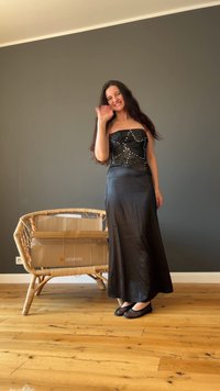 Μαύρο strapless φόρεμα με λαμπερά, διακοσμημένα αξεσουάρ, απαλής σατέν υφής, μακρύς σχεδιασμός. Φορεμένο με μαύρα δίκτυα φλατ παπούτσια. Φόντο με ξύλινο δάπεδο.