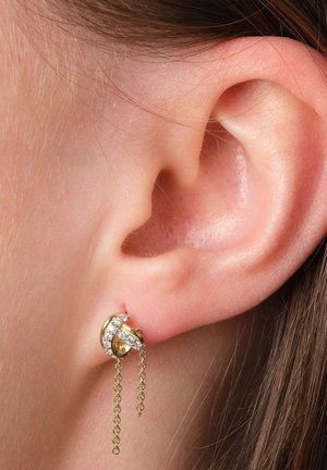 Ohrringe in Goldfarbe mit einem kreisförmigen Design, verziert mit funkelnden Kristallen und zarten Kettenakzenten. Strukturiert mit einer polierten Oberfläche.