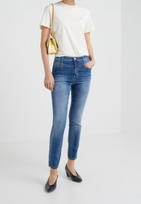 Ljusblå skinny jeans i denim med medelhög midja, bärs med en vit T-shirt och en liten guldkvot. Glansiga marinblå klackar fulländar outfiten.