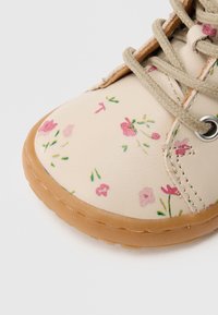 Μπεζ δερμάτινο παπούτσι με λουλουδένιο σχέδιο σε ροζ και πράσινο, με στρογγυλή μύτη, λάστιχο σόλα και μπεζ κορδόνια μέσα από μεταλλικά πλαϊνά.