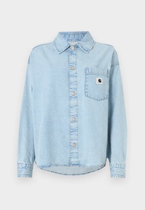 Camicia di denim azzurro chiaro con tasca frontale, chiusura con bottoni e maniche lunghe. Presenta una toppa con il logo sulla tasca e cuciture visibili.