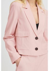 Krátké růžové sako z texturované látky s výstřihem s klopy, dvěma předními kapsami a dvěma tmavými knoflíky na zapínání.